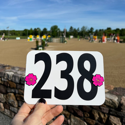 pinsnickety pink poppy horse show number pins on a show number in front of a jumper arena