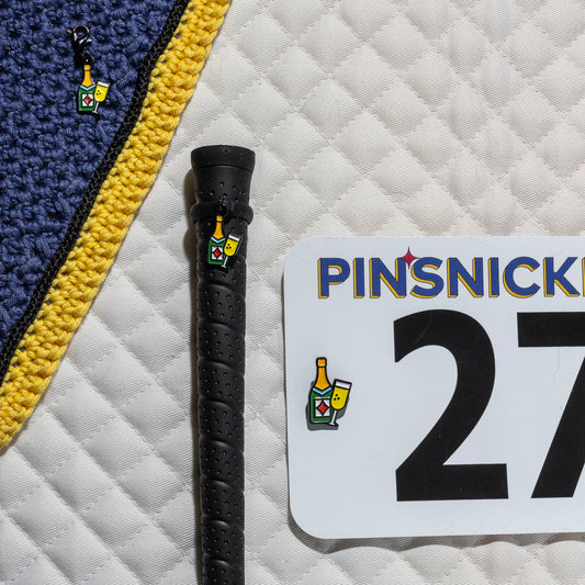 A saddle pad, bonnet and whip decorated with matching Champagne Pinsnickety horse show number pins, a bridle charm and a crop charm.