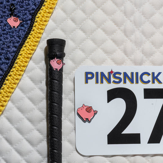 A saddle pad, bonnet and whip decorated with matching Flying Pig Pinsnickety horse show number pins, a bridle charm and a crop charm.
