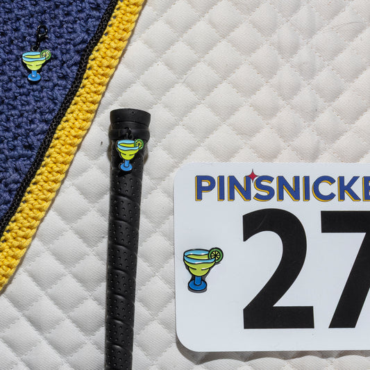 A saddle pad, bonnet and whip decorated with matching Margarita Pinsnickety horse show number pins, a bridle charm and a crop charm.