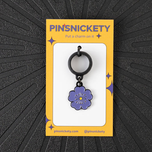 a pinsnickety purple poppy crop charm on its yellow product packaging card in front of a black background