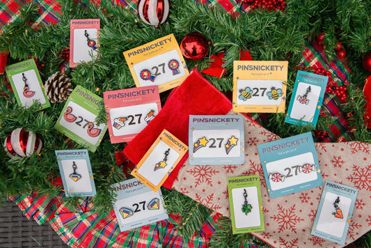 a selection of pinsnickety horse show pins and charms on colored cards strewn atop holiday directions, including a stocking and christmas ornaments