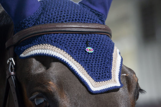 a close up of a horse wearing a blue fly bonnet decorated with a pinsnickety BOOM! bridle charm