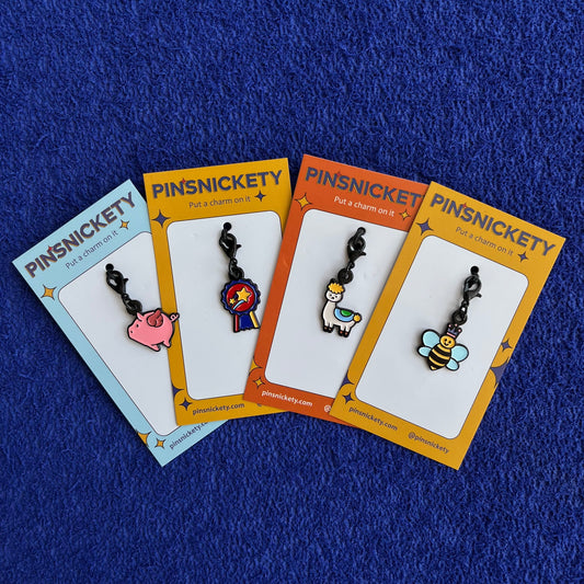 Pinsnickety flying pig, champion, drama llama, and queen bee braid and bridle horse show charms on a blue background