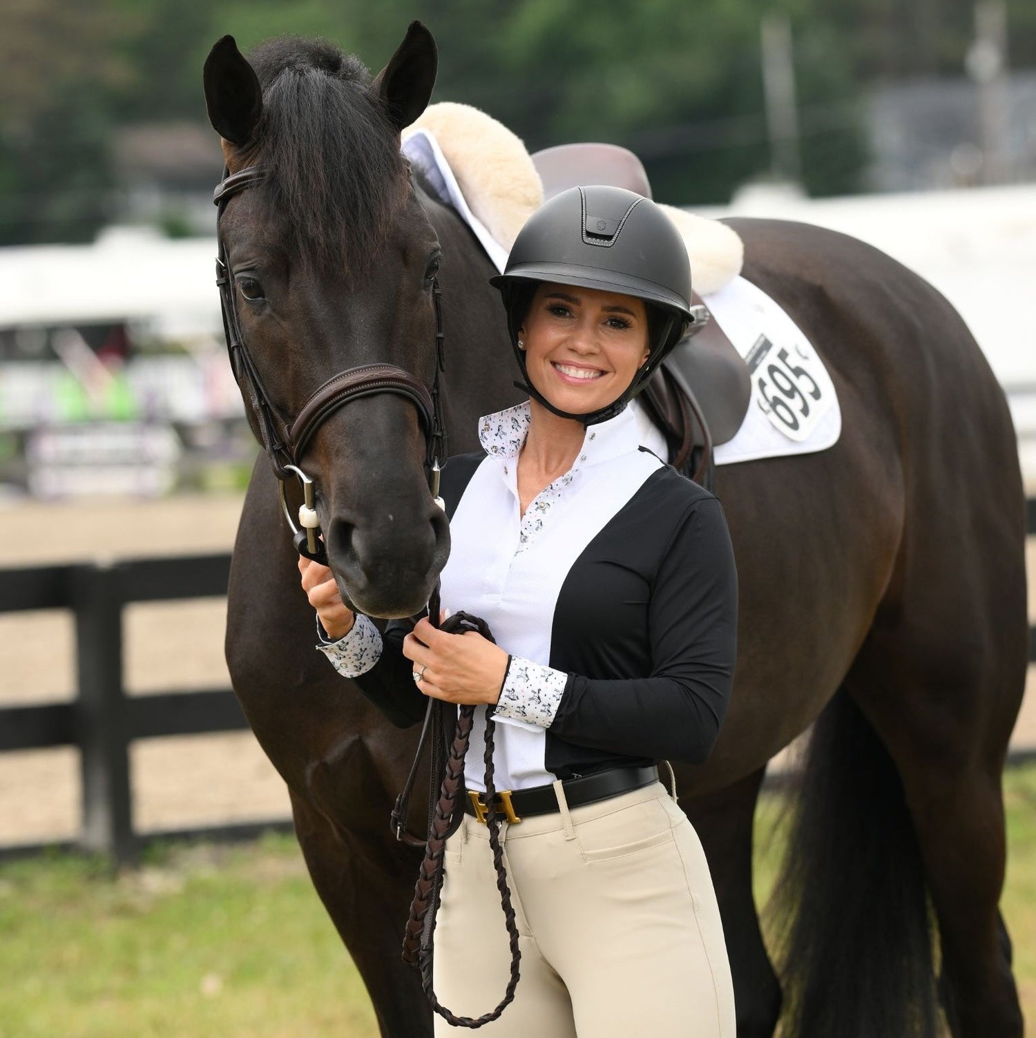 A woman wearing an essex classics show shirt holds a horse wearing a show number attached with matching Pinsnickety unicorn horse show number pins