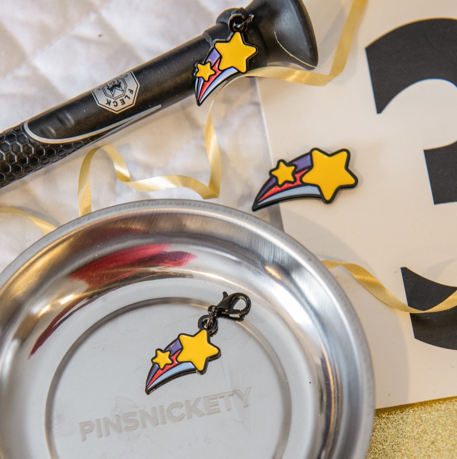 A pinsnickety shooting star triple combination set with a crop charm on a whip handle, a horse show number pin attached to a saddle pad and a bridle charm sitting in a silver Pinsnickety magnetic storage bowl.
