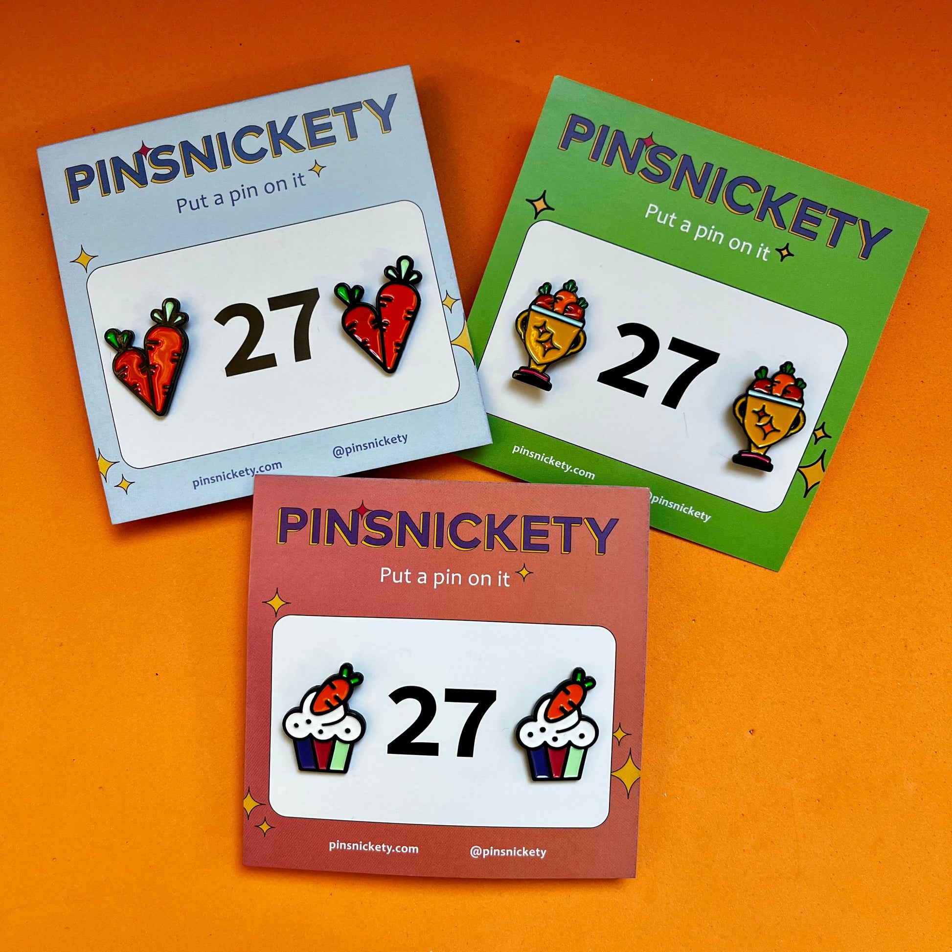 A pack of three pinsickety horse show number pin sets featuring carrots on an orange background. The shapes are Carrots, Trophies, and Cupcakes.