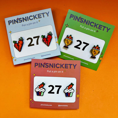 A pack of three pinsickety horse show number pin sets featuring carrots on an orange background. The shapes are Carrots, Trophies, and Cupcakes.