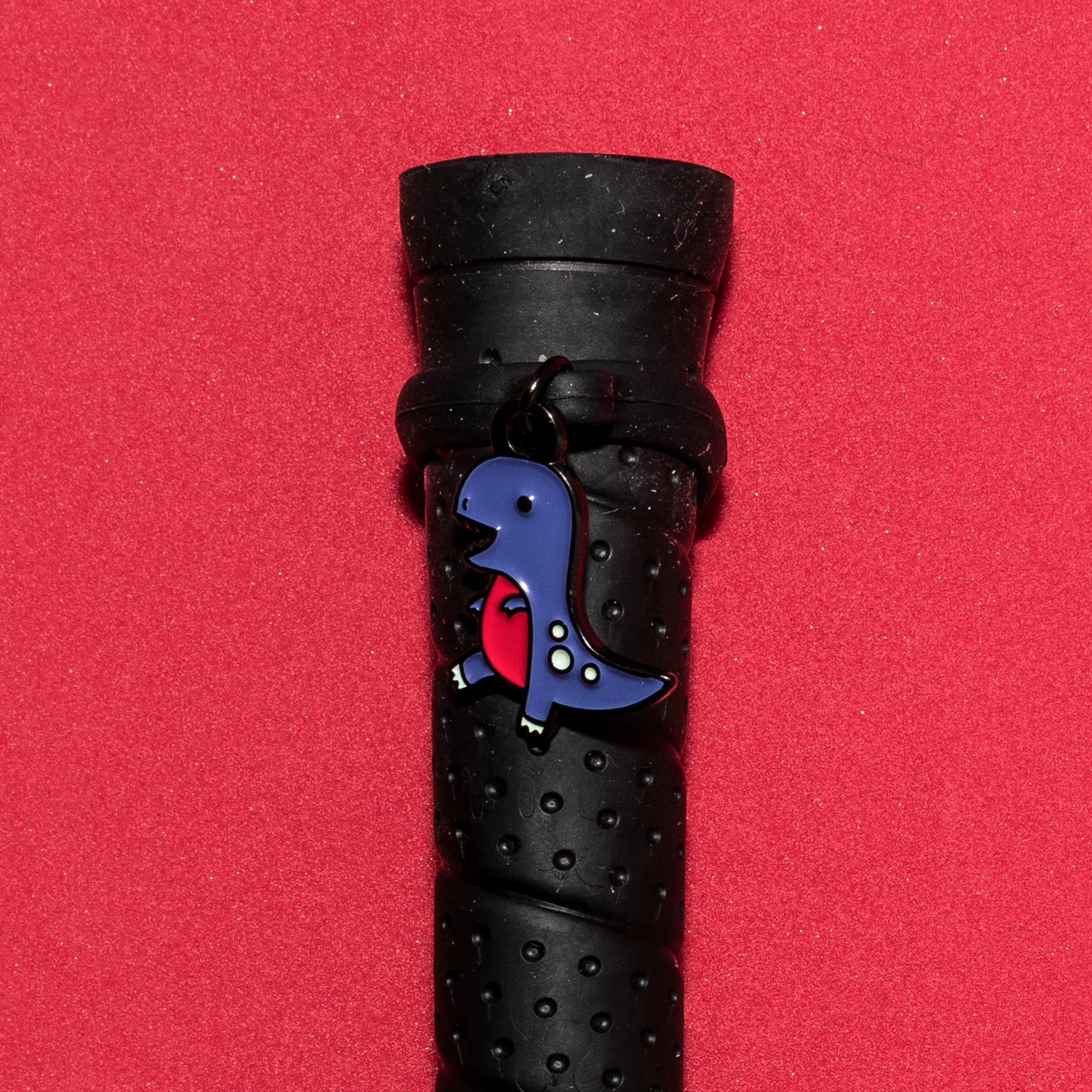 Pinsnickety T-Rex crop charm on a whip handle in front of a colored background