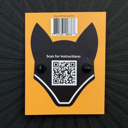 The yellow back of a Pinsnickety product packaging card with an illustration of a jumper fly bonnet, showing the rubber pin clasps of the back off red ribbon bonnet pin, a QR code, and a UPC code.