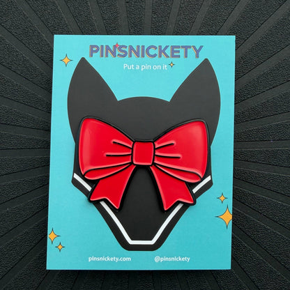 A back off red ribbon enamel bonnet pin displayed on a teal Pinsnickety card with an illustration of a jumper fly bonnet, set on a black textured background.
