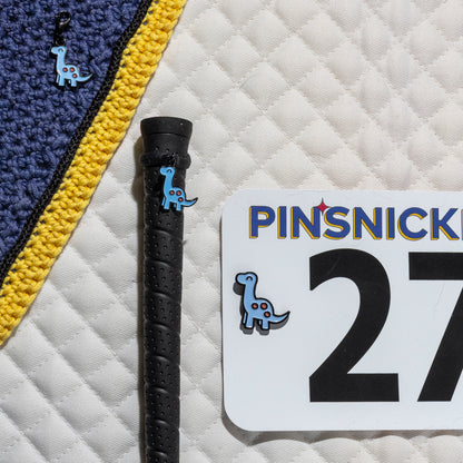 A saddle pad, bonnet and whip decorated with matching Brontosaurus Pinsnickety horse show number pins, a bridle charm and a crop charm.