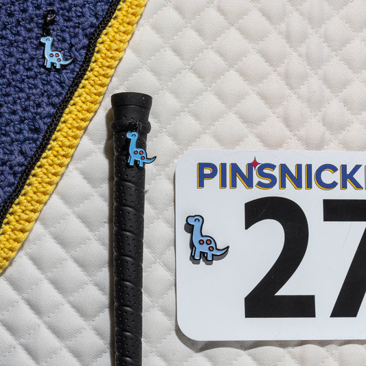 A saddle pad, bonnet and whip decorated with matching Brontosaurus Pinsnickety horse show number pins, a bridle charm and a crop charm.
