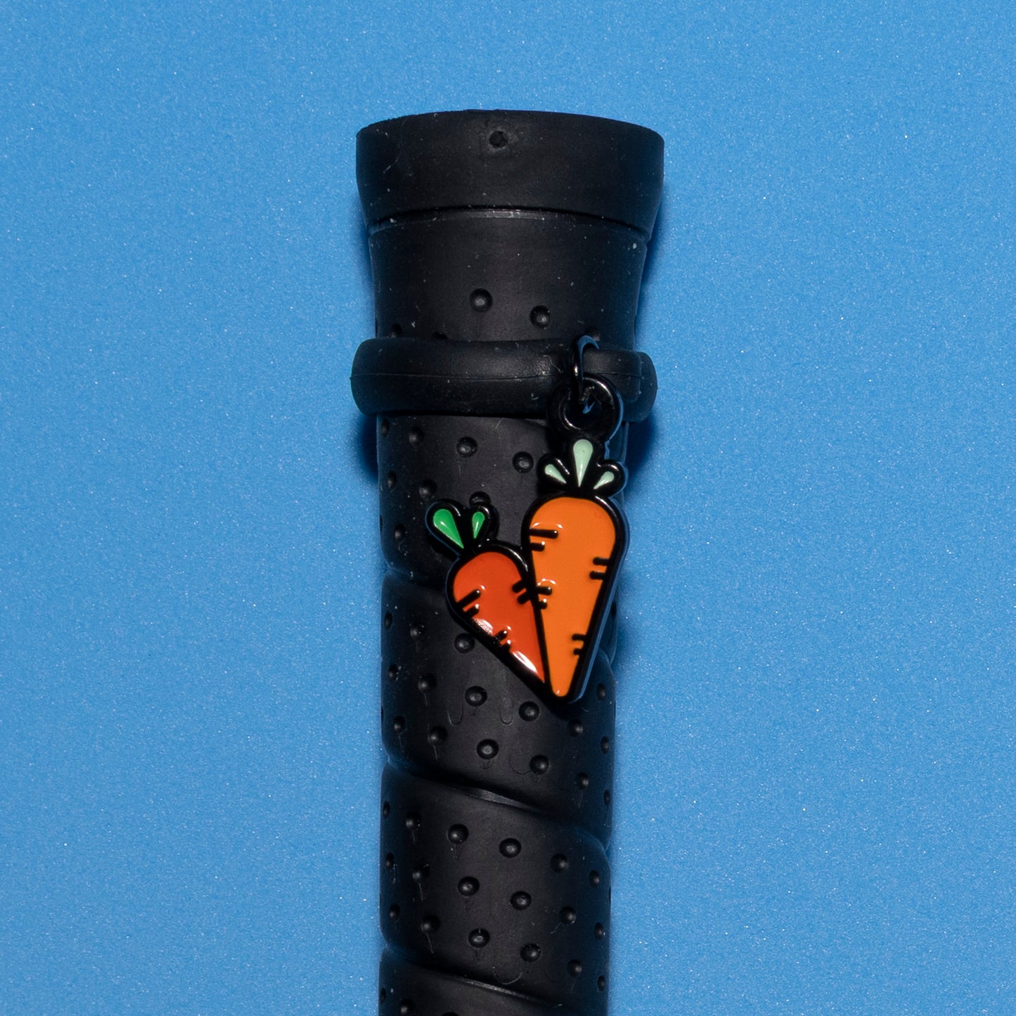 Pinsnickety Carrots crop charm on a whip handle in front of a colored background