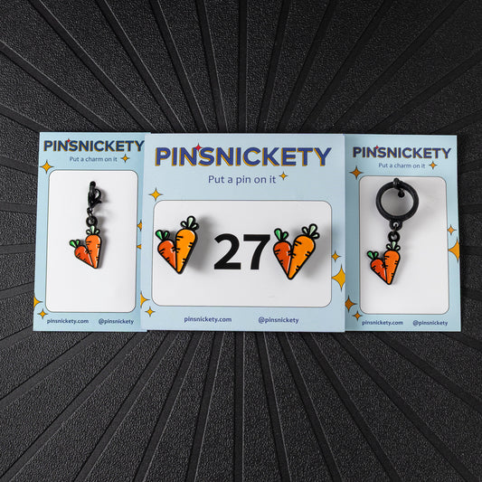 A matching triple combination set with Pinsnickety Carrots horse show number pins, a bridle charm, and a crop charm in their product packaging on a black background.