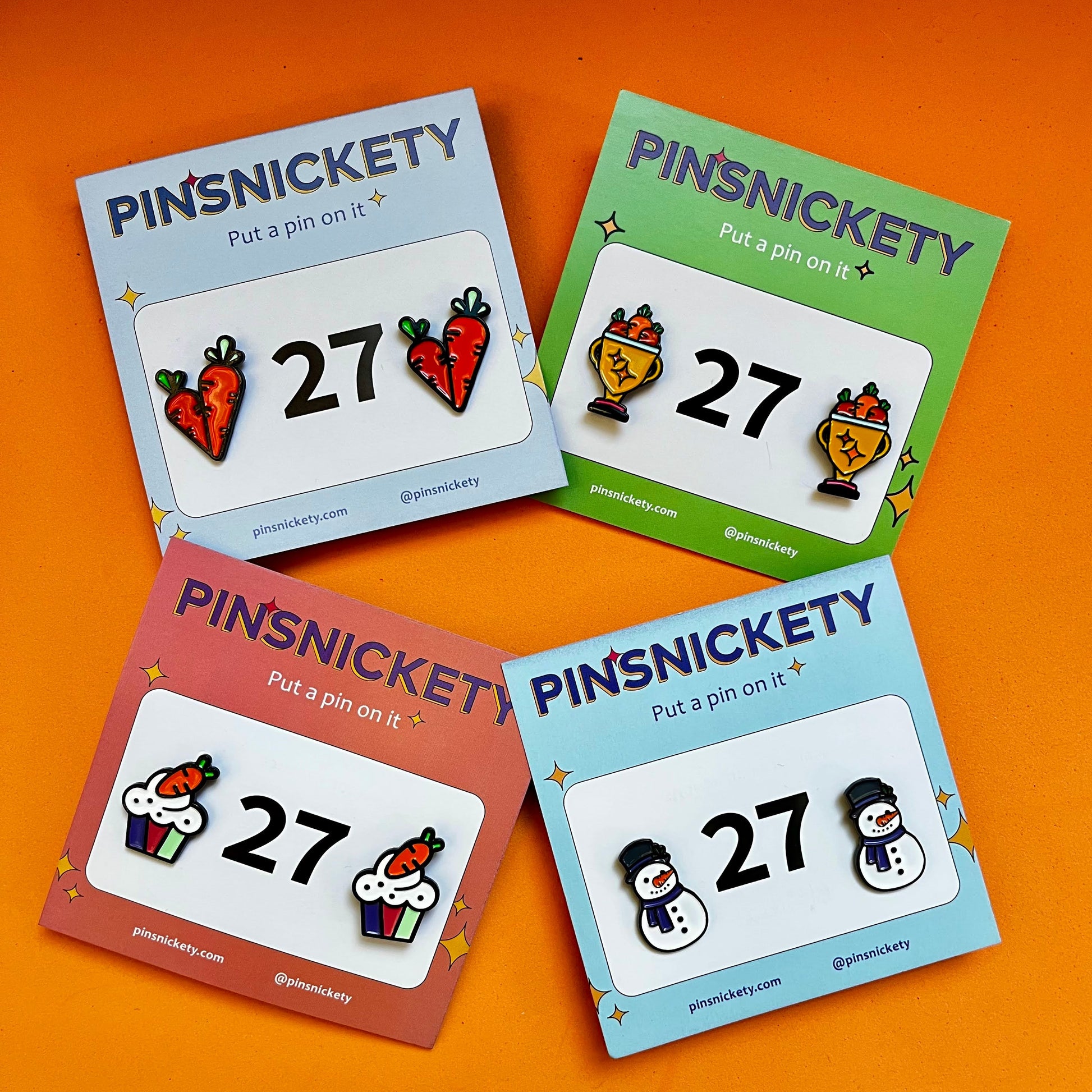 four sets of Pinsnickety horse show number pins including carrots on an orange background.