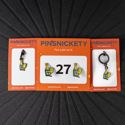 A matching triple combination set with Pinsnickety Champagne horse show number pins, a bridle charm, and a crop charm in their product packaging on a black background.