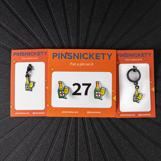 A matching triple combination set with Pinsnickety Champagne horse show number pins, a bridle charm, and a crop charm in their product packaging on a black background.