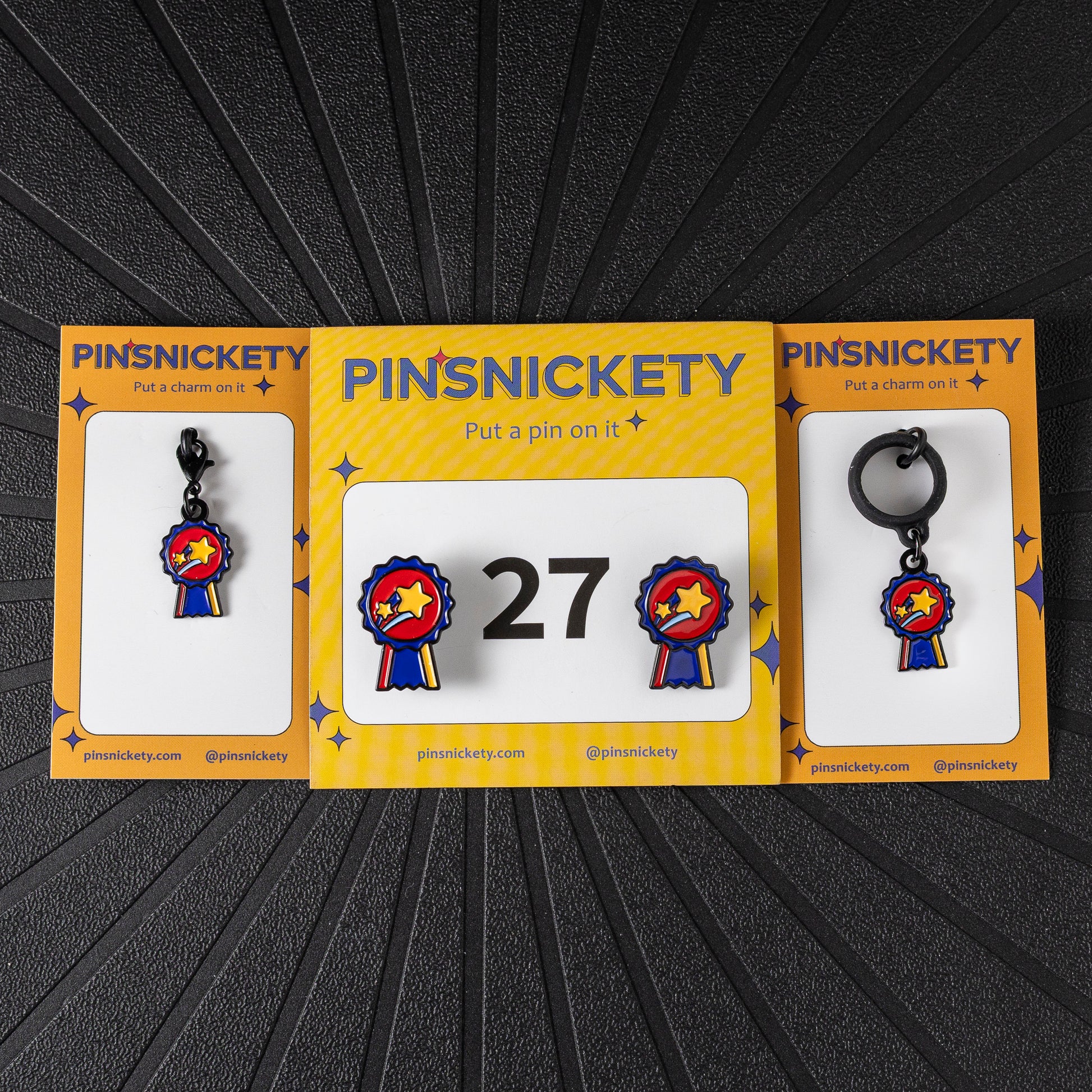 A matching triple combination set with Pinsnickety Champion horse show number pins, a bridle charm, and a crop charm in their product packaging on a black background.