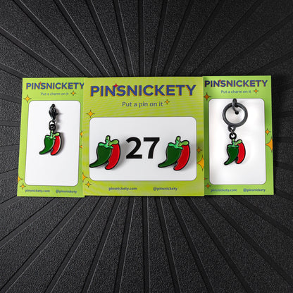 A matching triple combination set with Pinsnickety Chili Peppers horse show number pins, a bridle charm, and a crop charm in their product packaging on a black background.