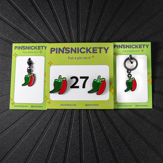 A matching triple combination set with Pinsnickety Chili Peppers horse show number pins, a bridle charm, and a crop charm in their product packaging on a black background.