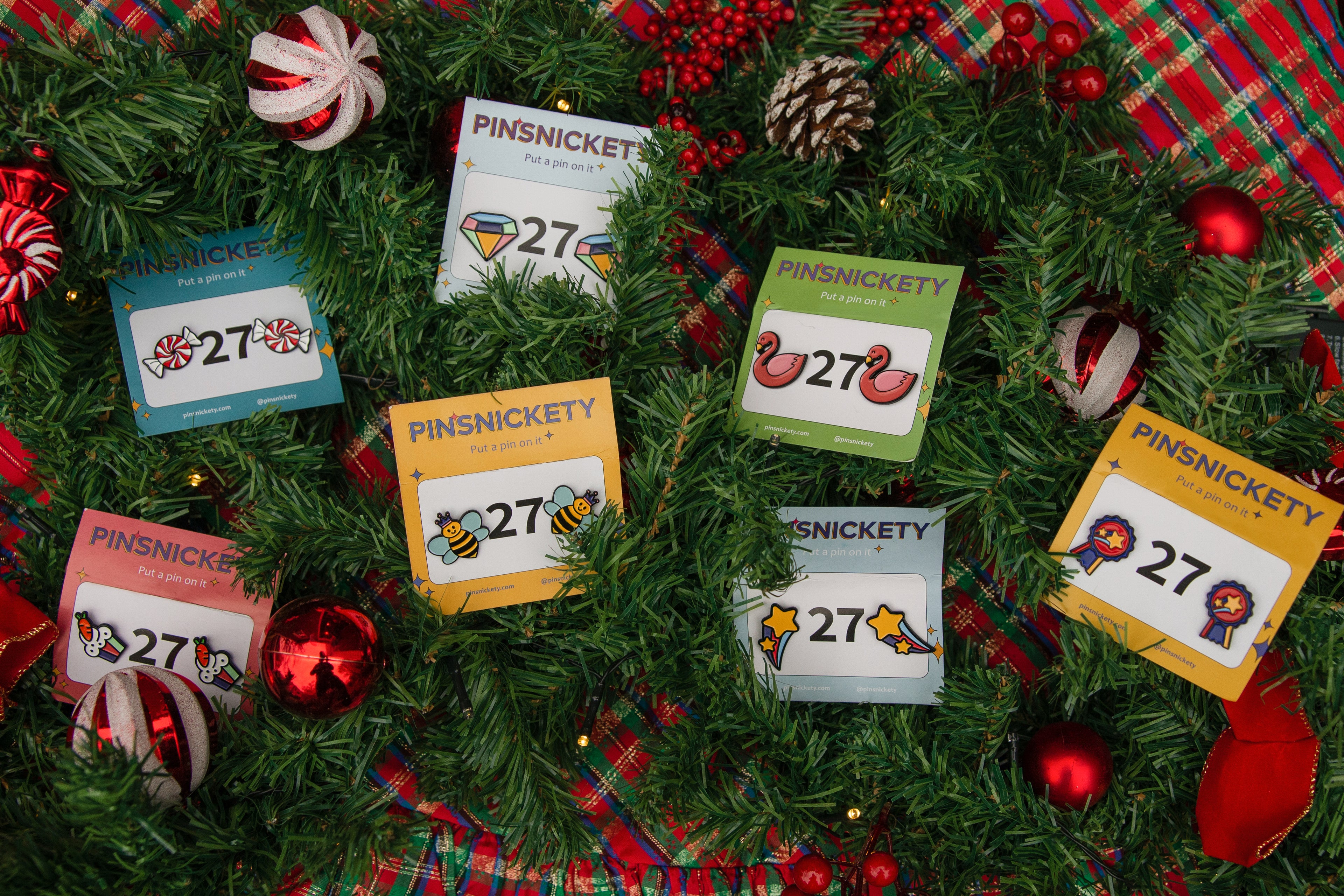 Pinsnickety horse show number pins on a background of evergreen branches, christmas ornaments and red plaid fabric.