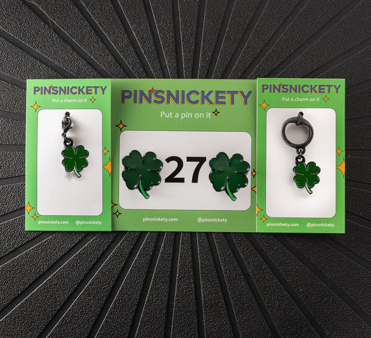 A matching triple combination set with Pinsnickety Clover horse show number pins, a bridle charm, and a crop charm in their product packaging on a black background.