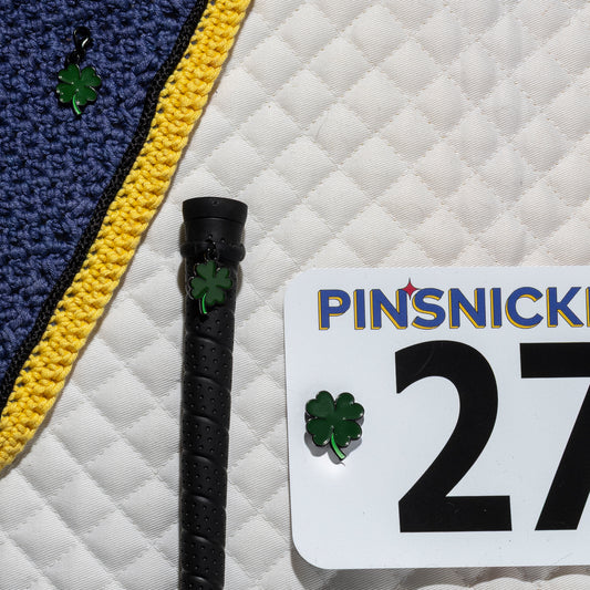 A saddle pad, bonnet and whip decorated with matching Clover Pinsnickety horse show number pins, a bridle charm and a crop charm.