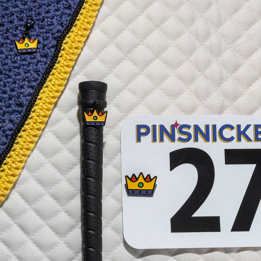 A saddle pad, bonnet and whip decorated with matching Crown Pinsnickety horse show number pins, a bridle charm and a crop charm.