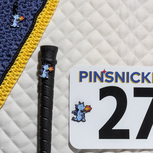 A saddle pad, bonnet and whip decorated with matching Dragon Pinsnickety horse show number pins, a bridle charm and a crop charm.