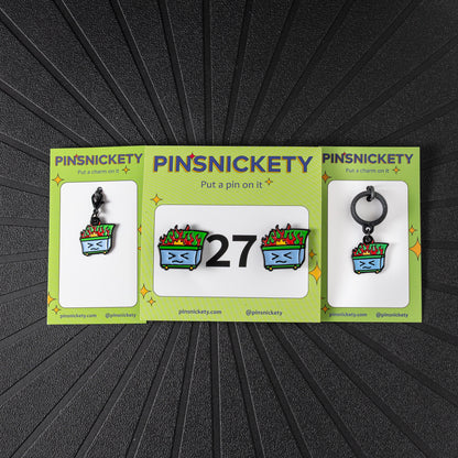 A matching triple combination set with Pinsnickety Dumpster Fire horse show number pins, a bridle charm, and a crop charm in their product packaging on a black background.
