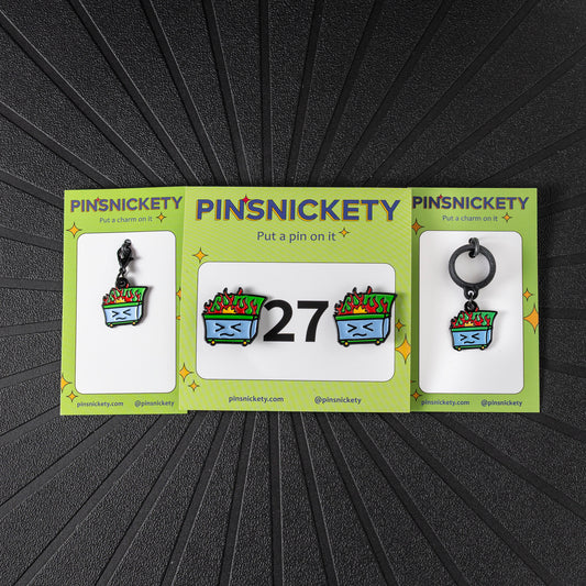 A matching triple combination set with Pinsnickety Dumpster Fire horse show number pins, a bridle charm, and a crop charm in their product packaging on a black background.