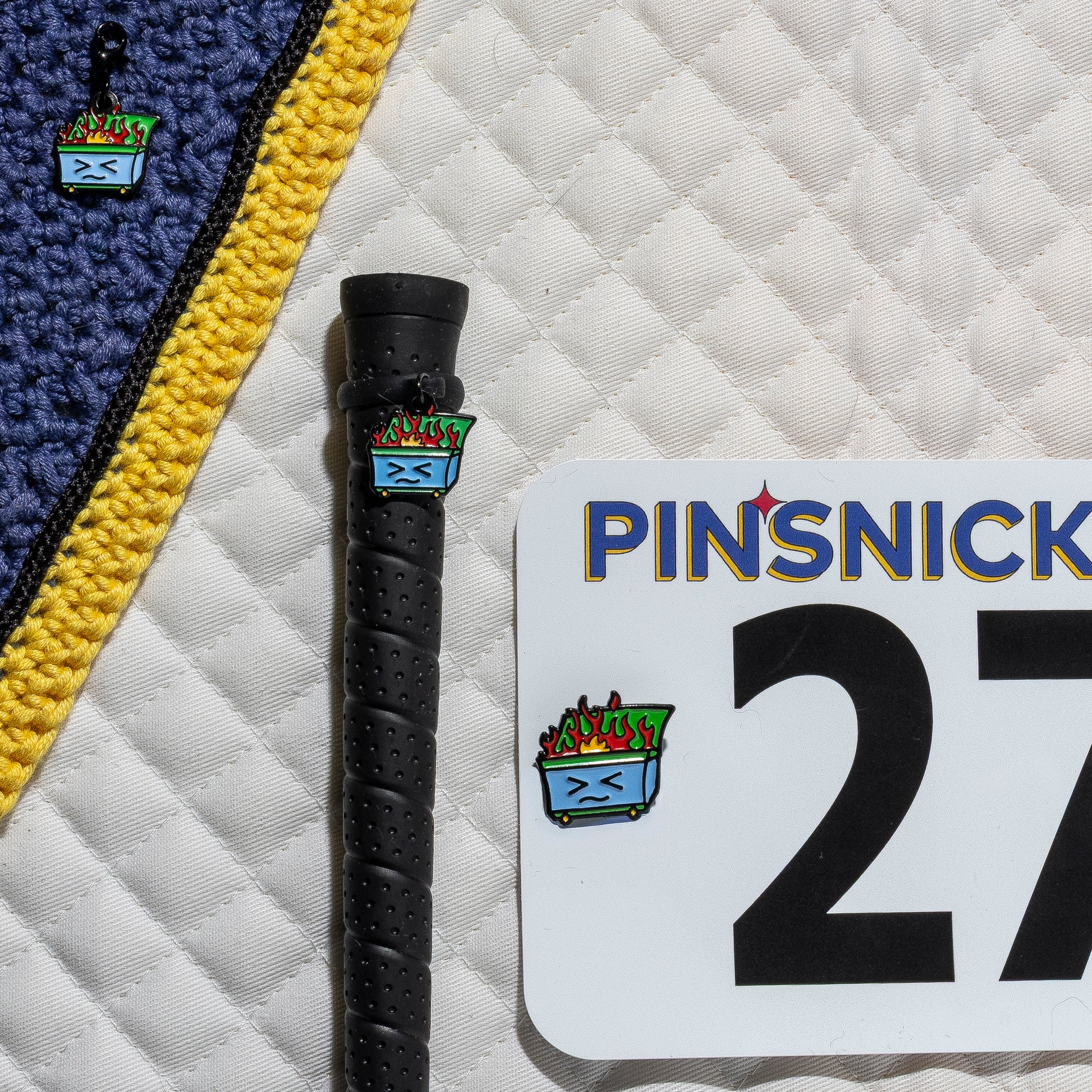 A saddle pad, bonnet and whip decorated with matching Dumpster Pinsnickety horse show number pins, a bridle charm and a crop charm.