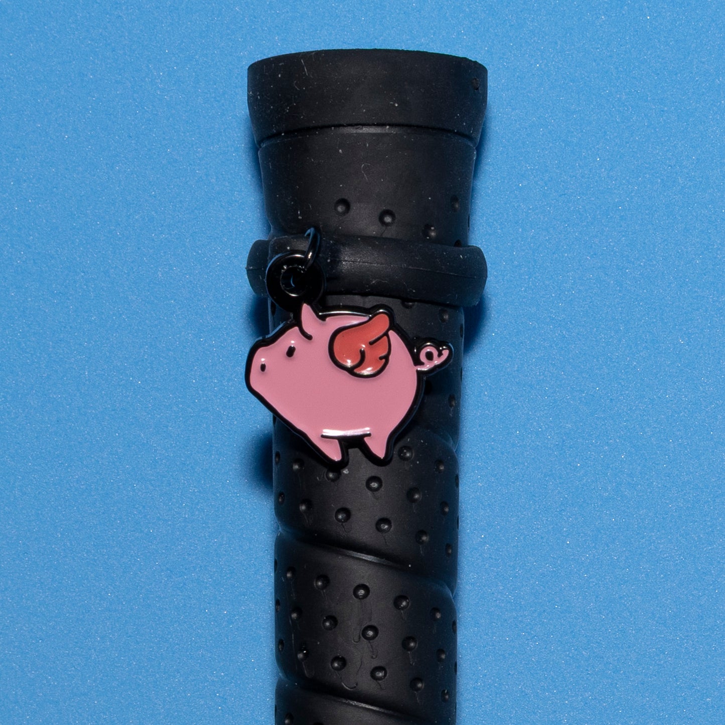 Pinsnickety Flying Pig crop charm on a whip handle in front of a colored background