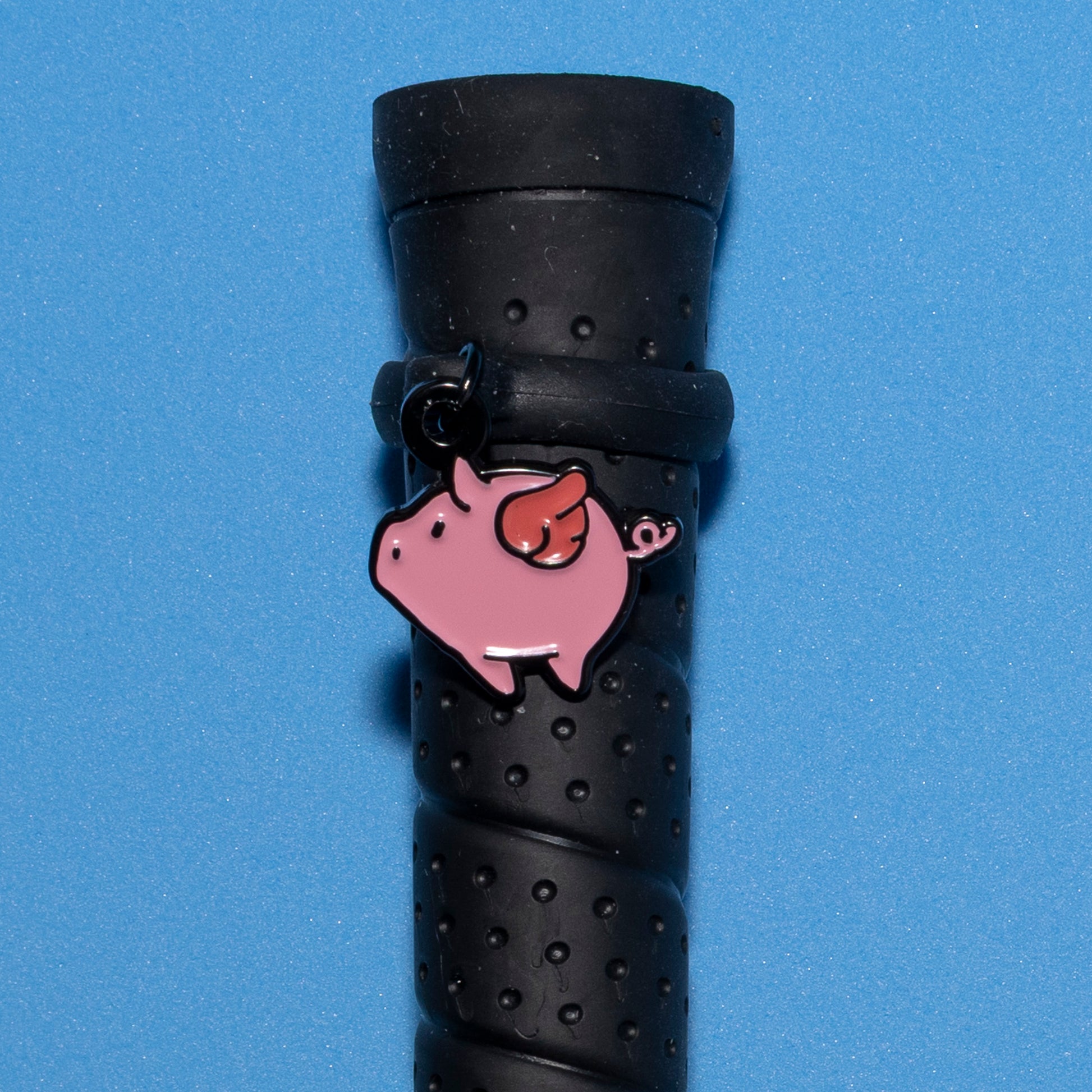 Pinsnickety Flying Pig crop charm on a whip handle in front of a colored background