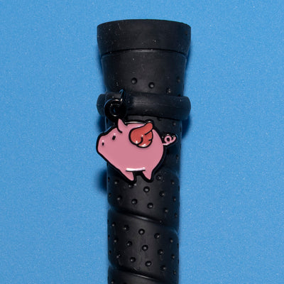 Pinsnickety Flying Pig crop charm on a whip handle in front of a colored background