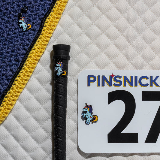 A saddle pad, bonnet and whip decorated with matching Flying Unicorn Pinsnickety horse show number pins, a bridle charm and a crop charm.
