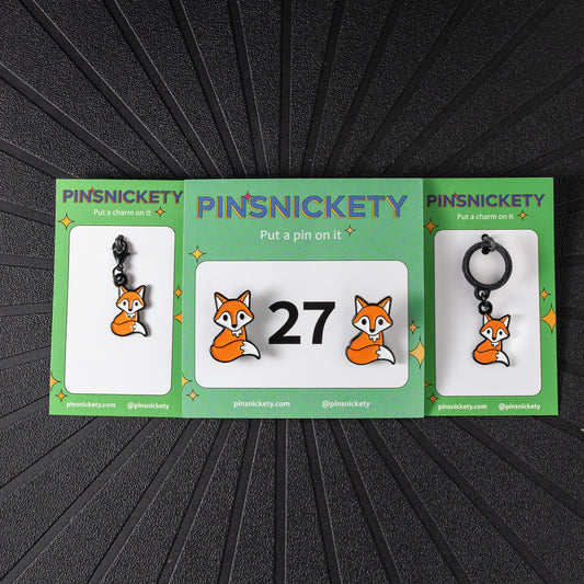 A matching triple combination set with Pinsnickety Fox horse show number pins, a bridle charm, and a crop charm in their product packaging on a black background.