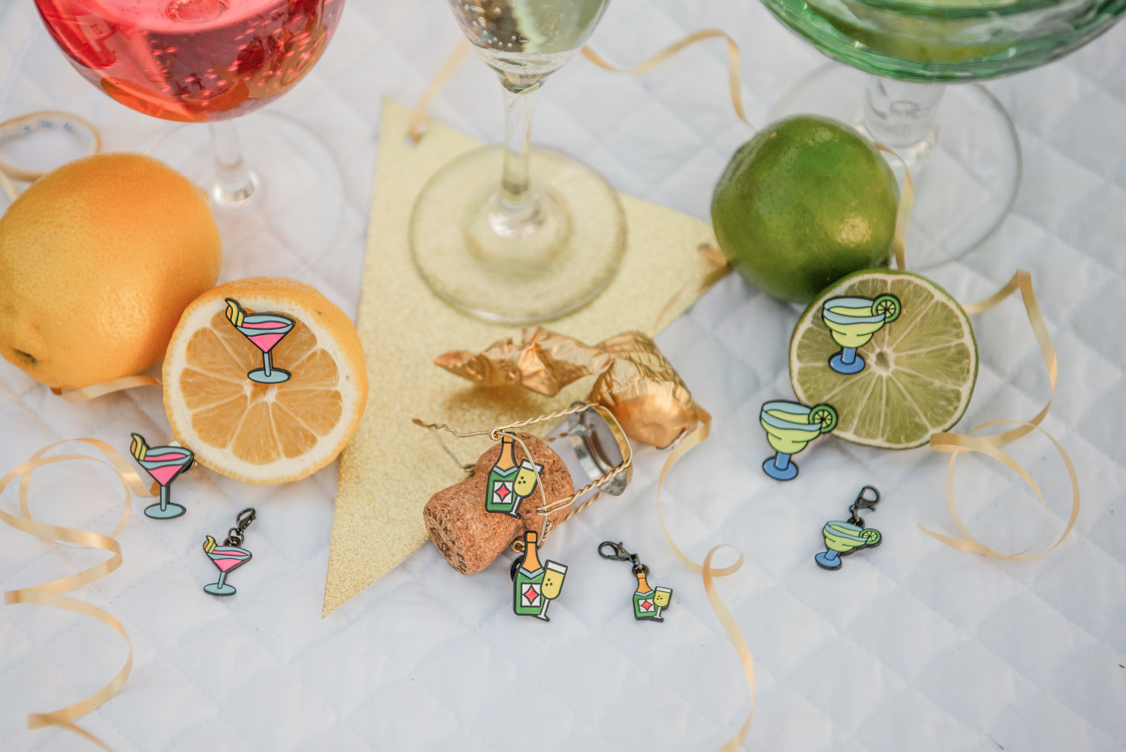 Decorative horse show number pins and bridle charms in the shape of cocktails and a cork with a lime and orange on a white saddle pad.