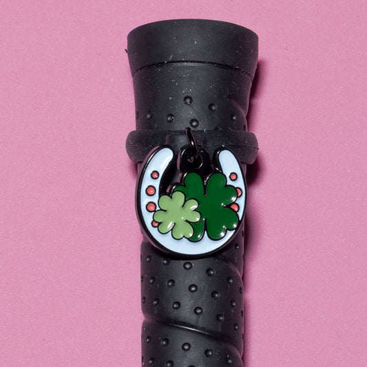 Pinsnickety Horseshoe crop charm on a whip handle in front of a colored background