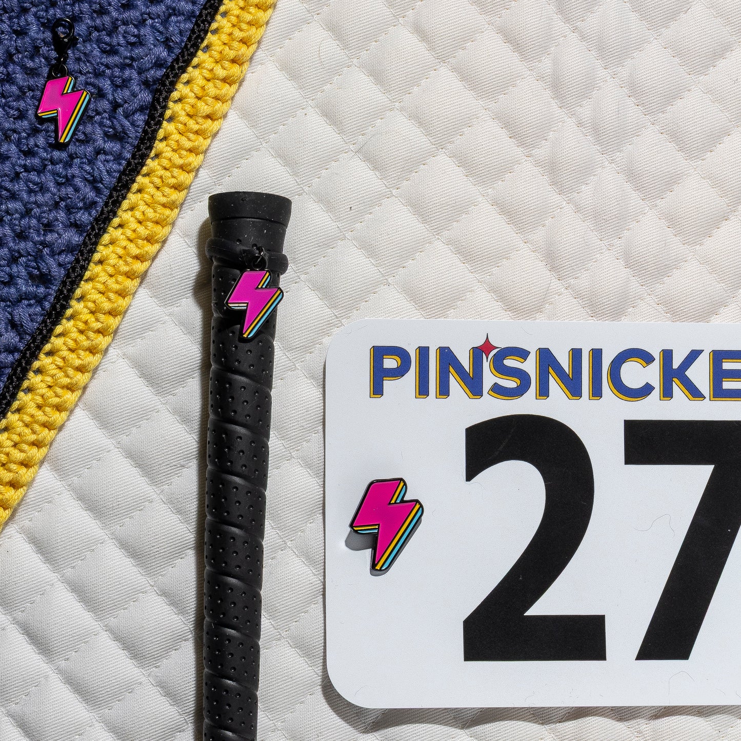 A saddle pad, bonnet and whip decorated with matching Lighning Bolt Pinsnickety horse show number pins, a bridle charm and a crop charm.