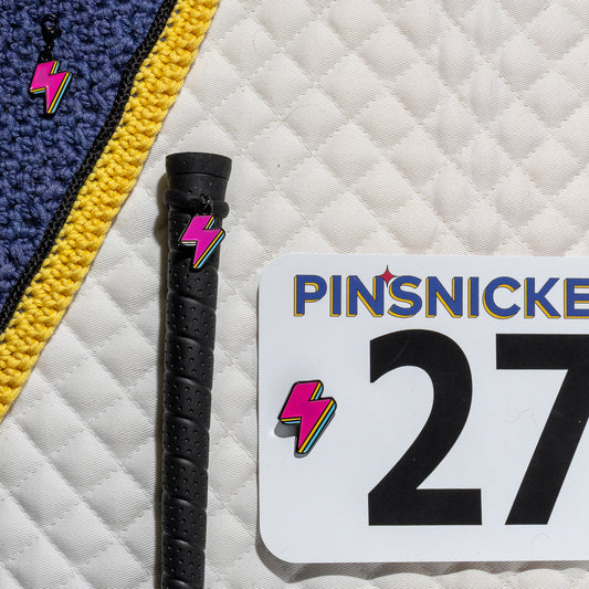 A saddle pad, bonnet and whip decorated with matching Lighning Bolt Pinsnickety horse show number pins, a bridle charm and a crop charm.