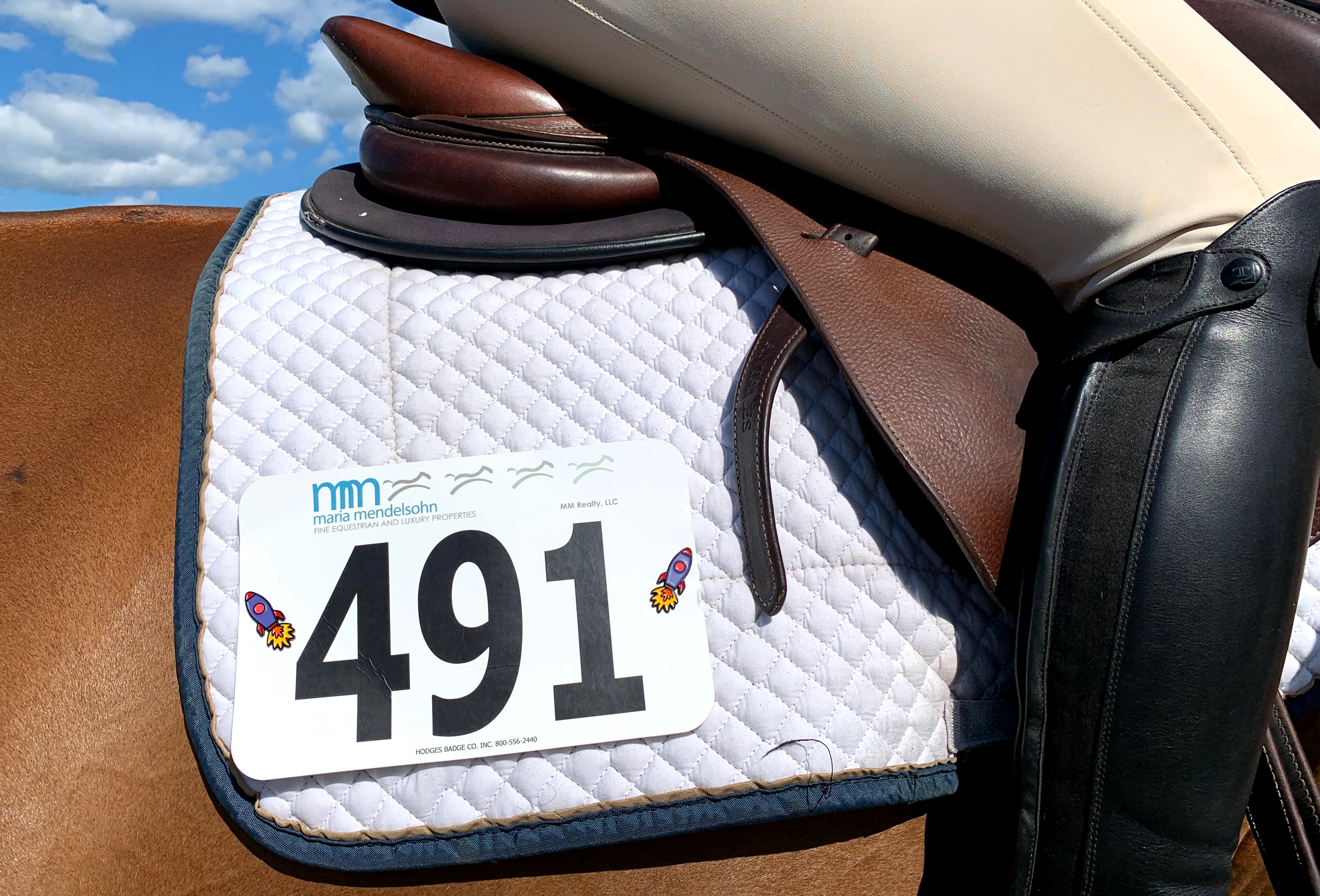 pinsnickety rocket ship horse show number pins on a saddle pad with a rider