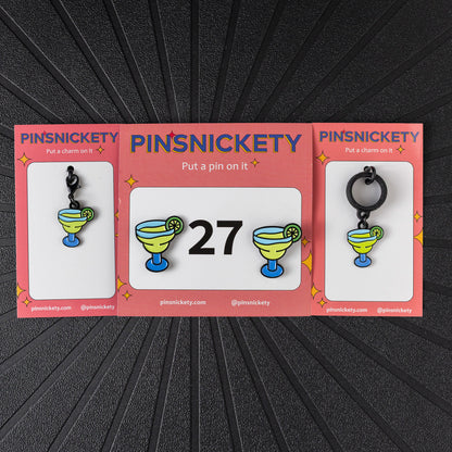 A matching triple combination set with Pinsnickety Margarita horse show number pins, a bridle charm, and a crop charm in their product packaging on a black background.