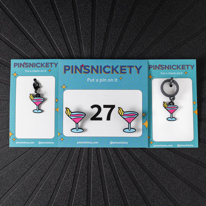 A matching triple combination set with Pinsnickety Martini horse show number pins, a bridle charm, and a crop charm in their product packaging on a black background.