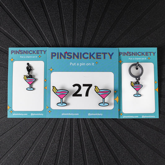 A matching triple combination set with Pinsnickety Martini horse show number pins, a bridle charm, and a crop charm in their product packaging on a black background.