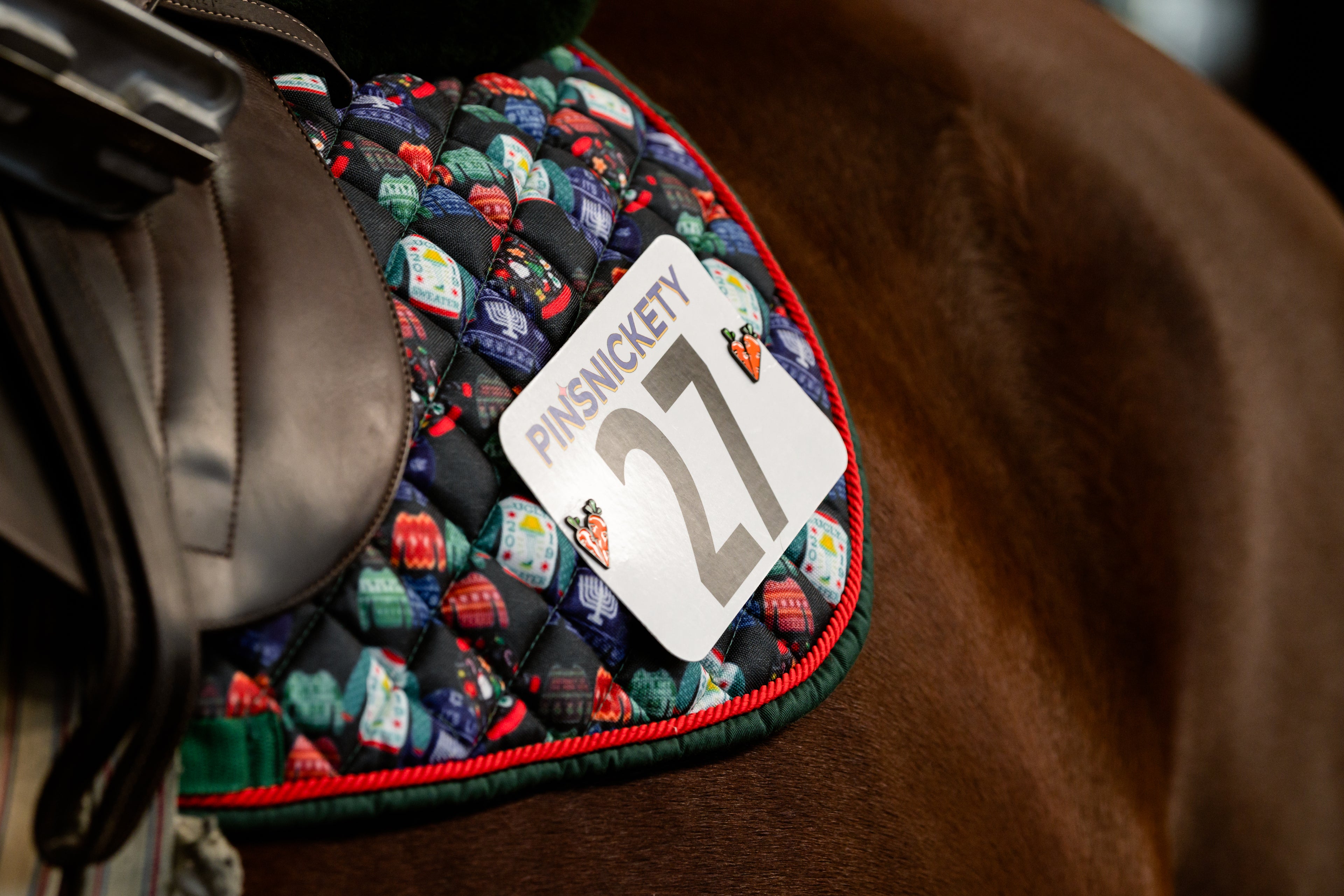 Pinsnickety carrots horse show number pins on a saddle pad decorated with holiday themed images