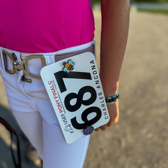 A closeup of the waistband of a rider using a Pinsnickety Queen Bee pin to attach their show number to their breeches for the jog at the USEF Pony Finals.