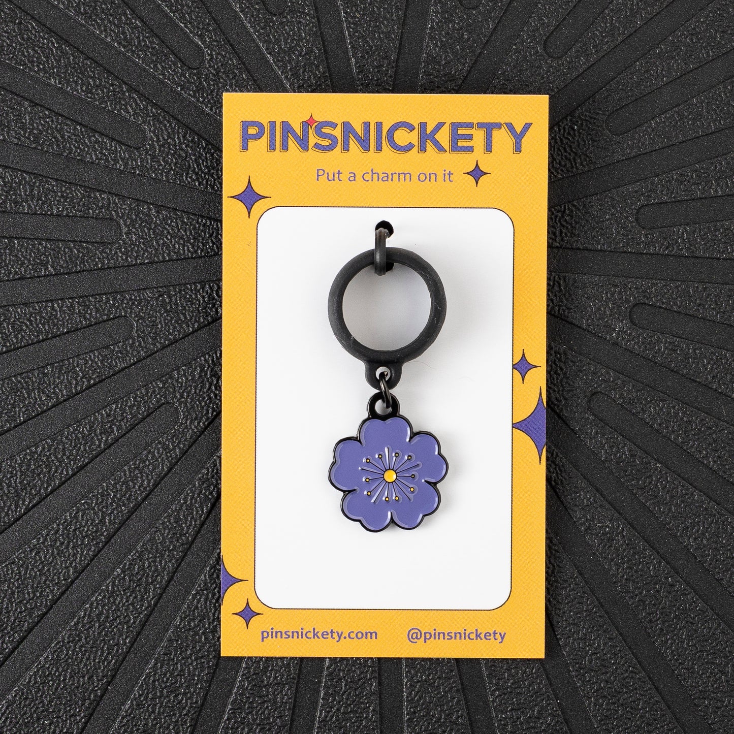 a pinsnickety purple poppy crop charm on its yellow product packaging card in front of a black background