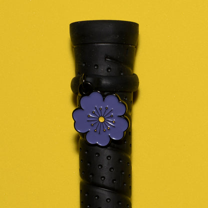 A close-up of a pinsnickety purple Poppy crop charm on a whip handle in front of a yellow background